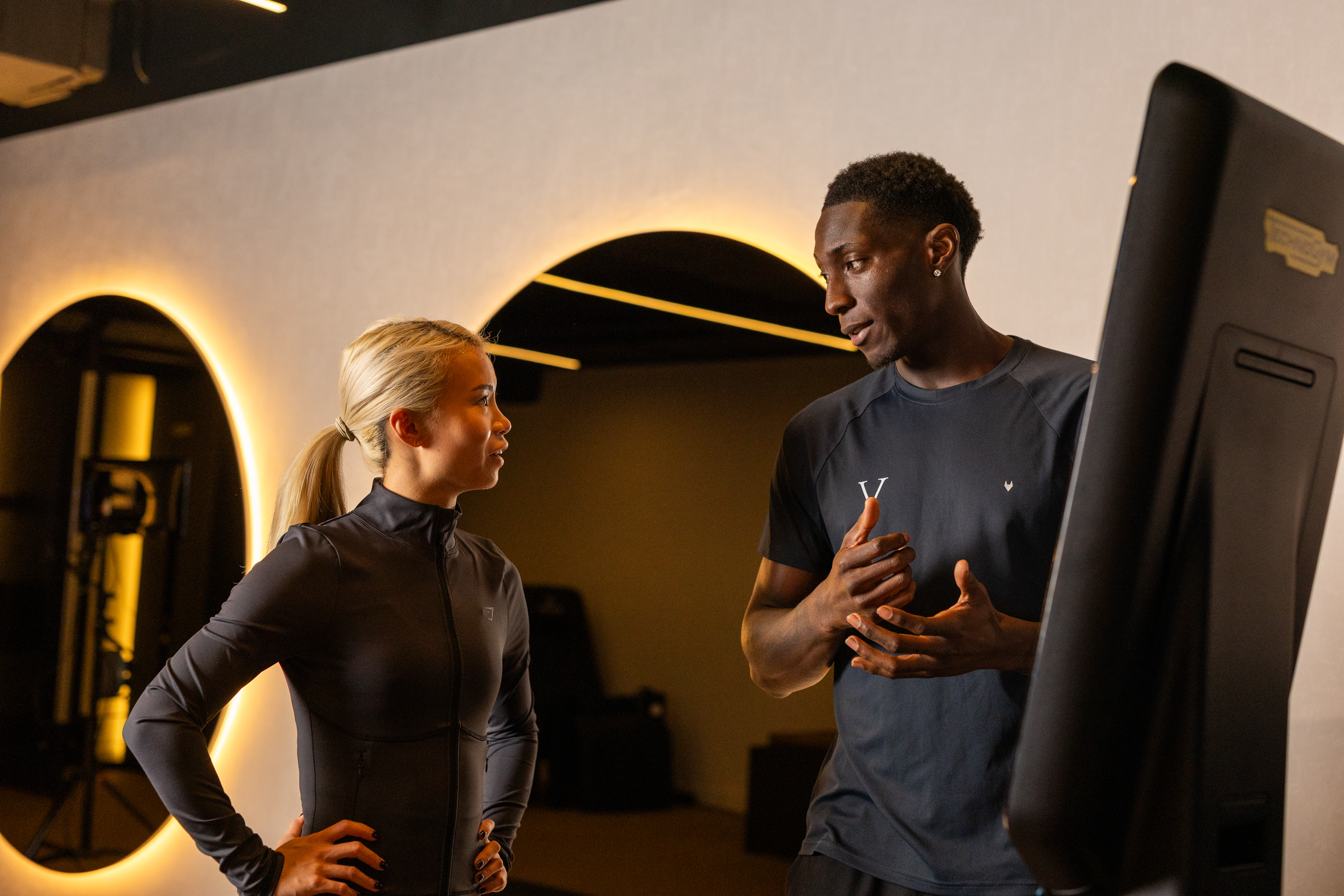 Personal Trainer with a client, talking through BMI results at a BMI machine located in the gym. 