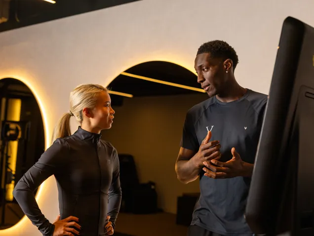 Personal Trainer with a client, talking through BMI results at a BMI machine located in the gym.